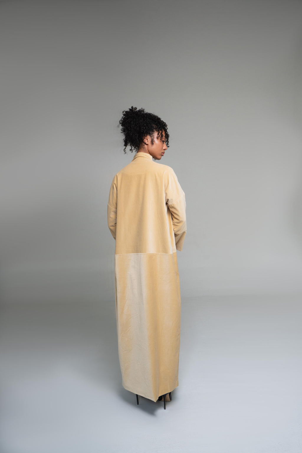 Person wearing a mustard yellow duster coat standing against a plain background
