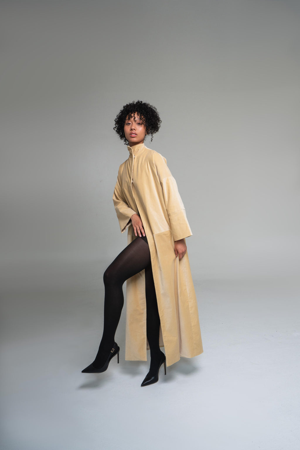 Woman wearing a mustard yellow duster coat on a plain background