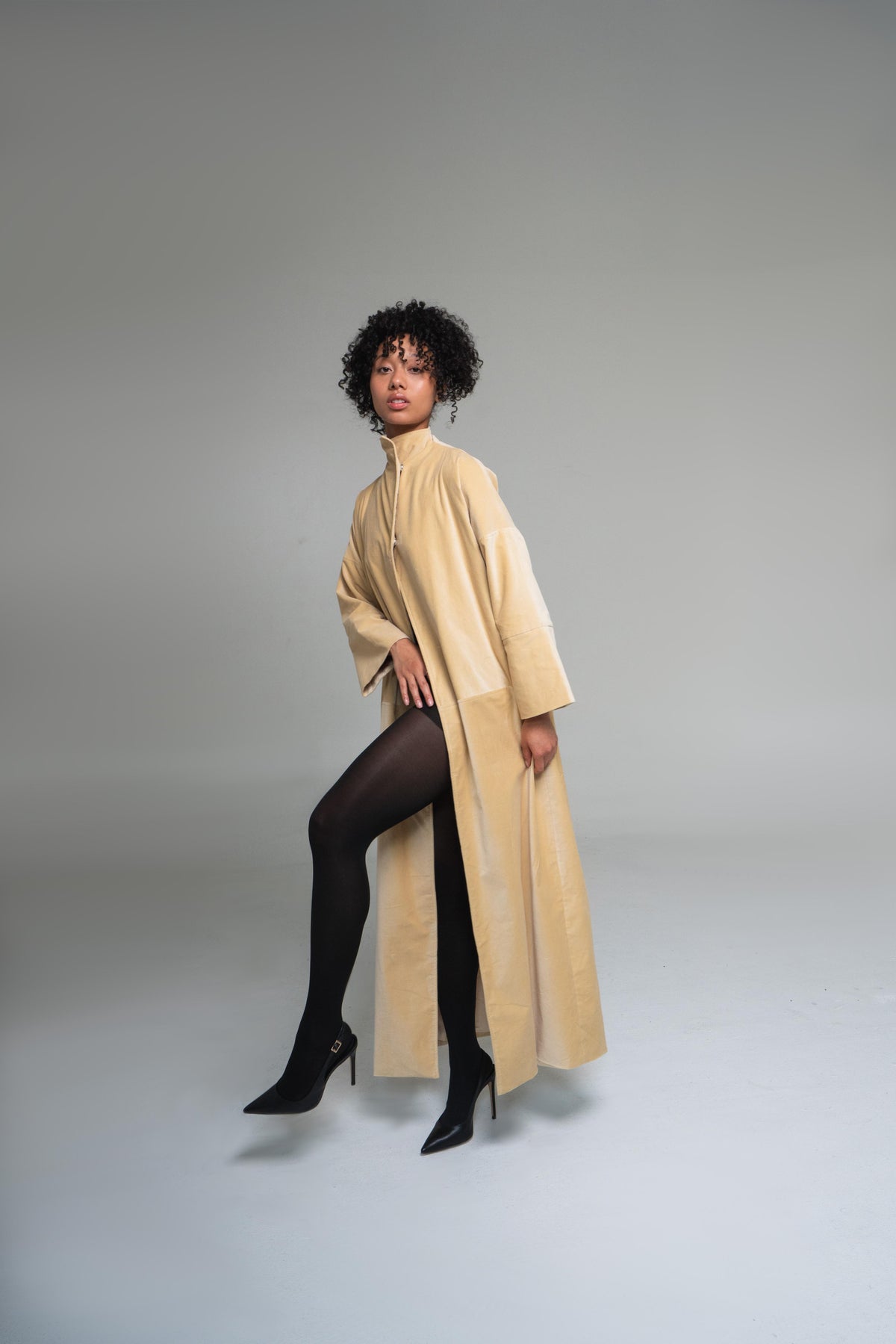 Woman wearing a mustard yellow duster coat on a plain background