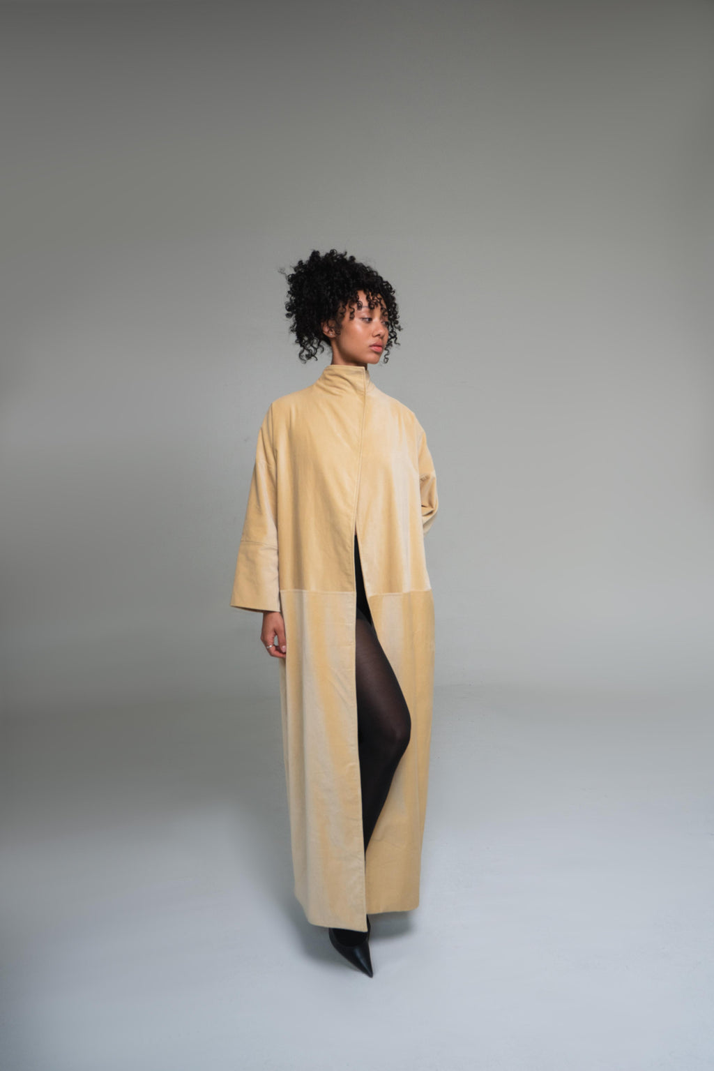 Woman wearing a mustard yellow duster coat on a gray background