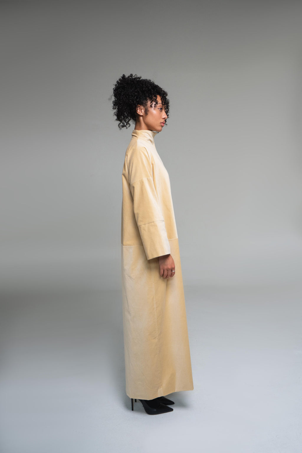 Person wearing a long mustard yellow duster coat against a gray background