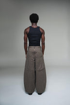 Person wearing a black tank top and plaid pants standing against a plain background