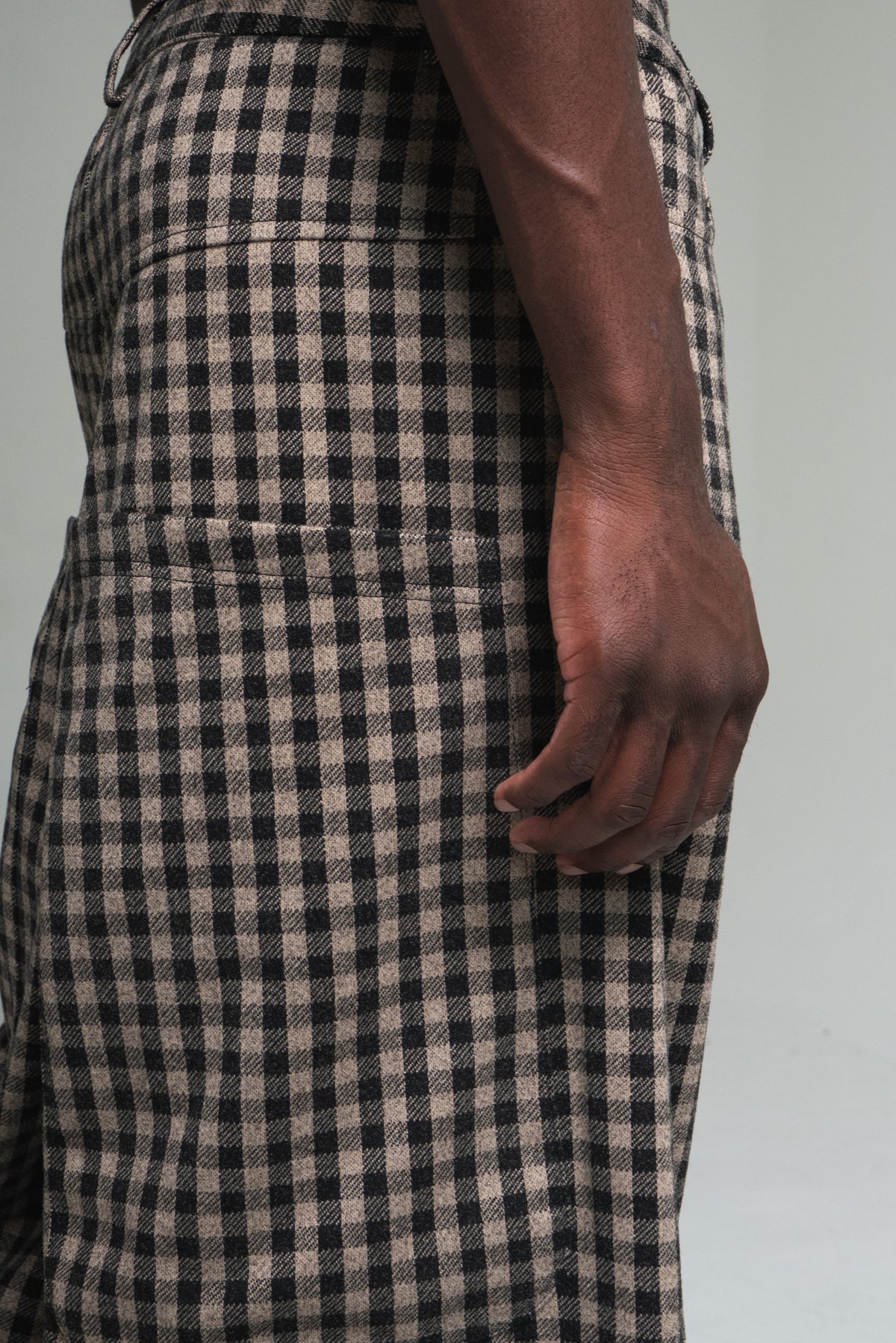Person wearing a black and brown checkered pant on a plain background