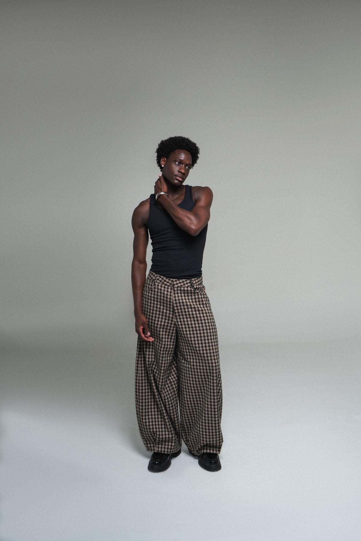 Person wearing a black tank top and plaid pants on a plain background