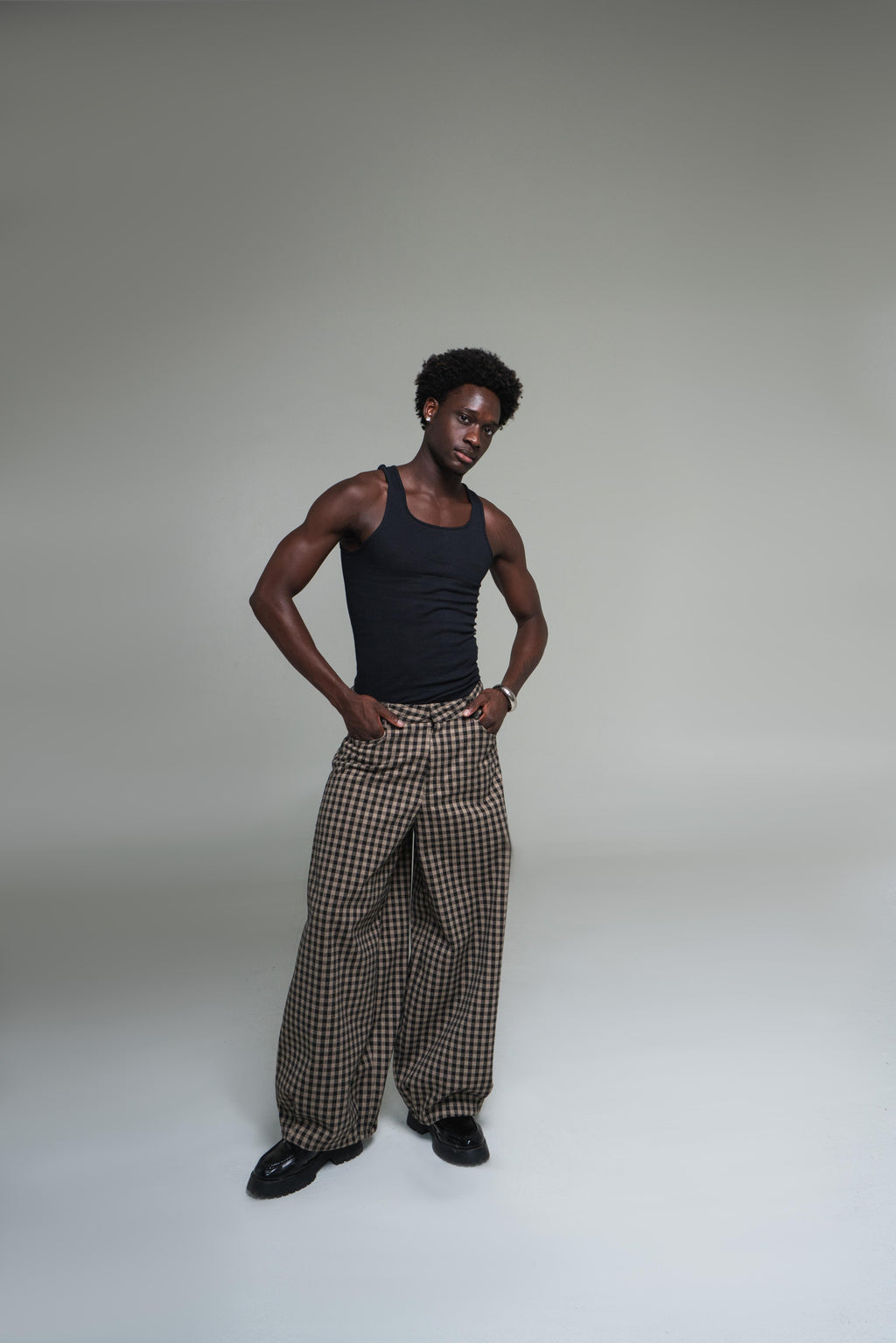 Man wearing a black tank top and plaid pants against a plain background