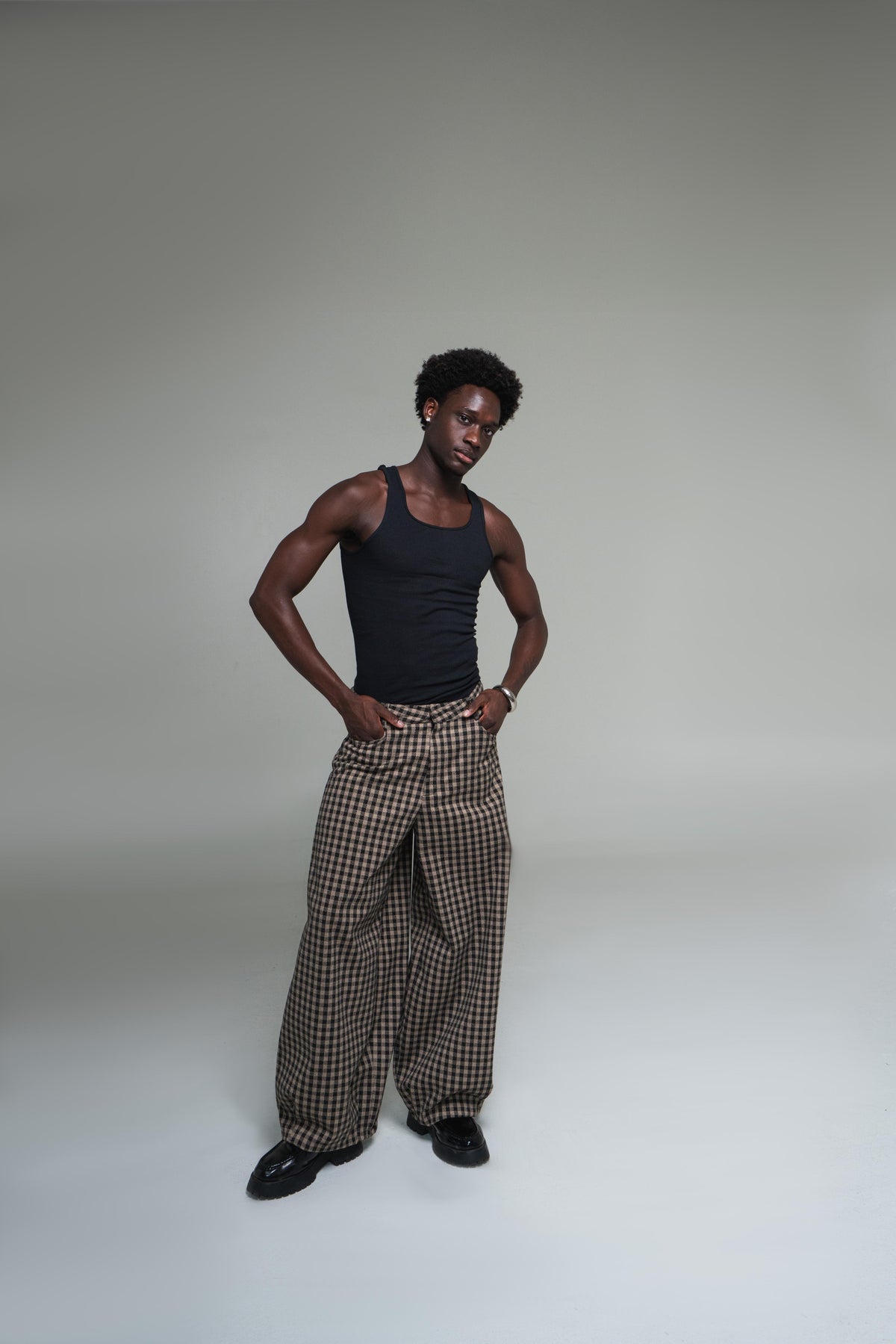 Man wearing a black tank top and plaid pants against a plain background