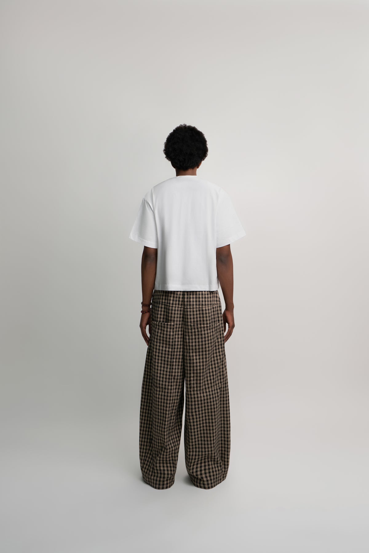 Person wearing a white t-shirt and plaid pants on a light gray background